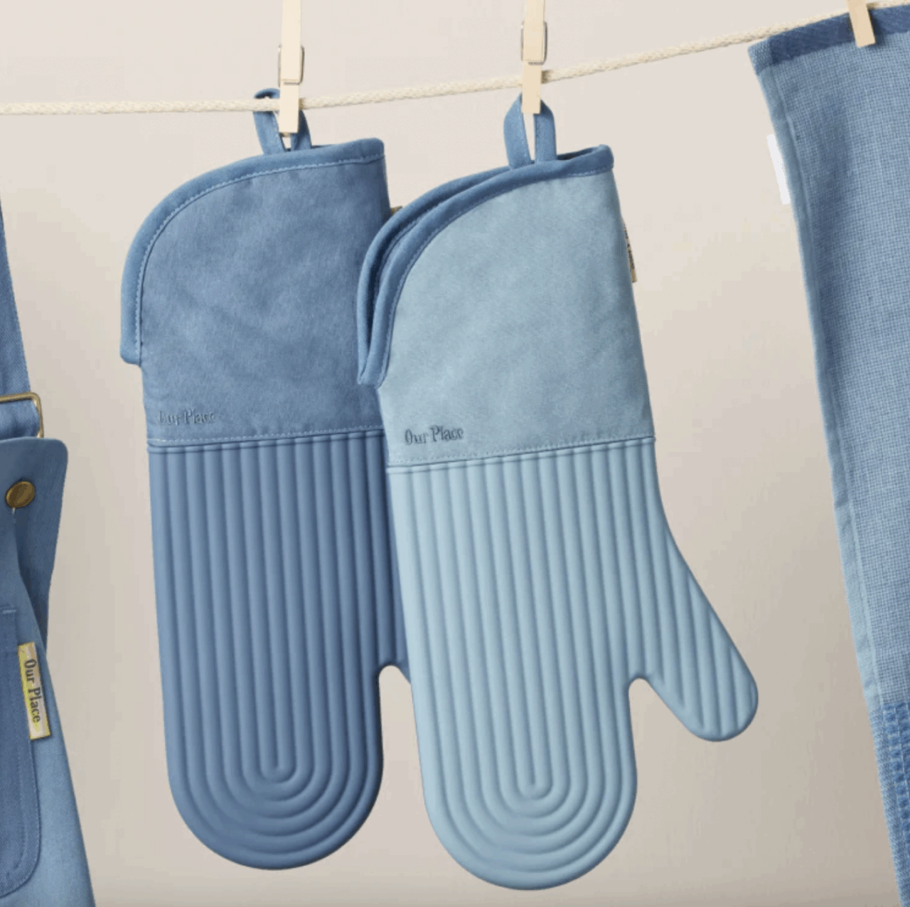 Image of two Our Place Hot Mitts in the color blue salt, hanging from a washing line.