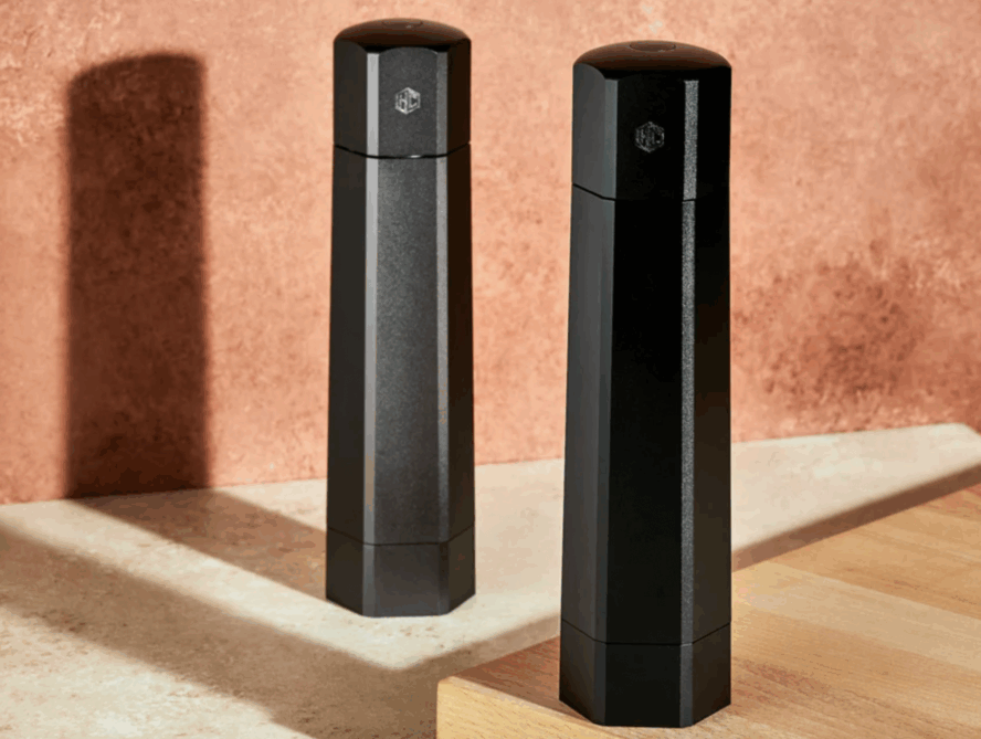 Image of the HexClad salt and pepper grinders against a terra cotta wallpaper background.