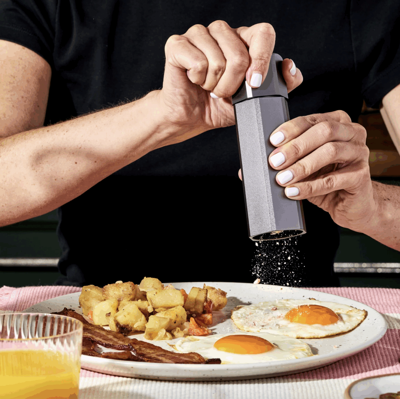 Image of someone using a HexClad salt grinder to salt eggs on a plate of breakfast foods.
