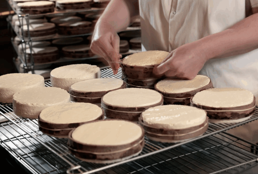 Image of a pair of hands wrapping a shelf of Winnimere cheese wheels.