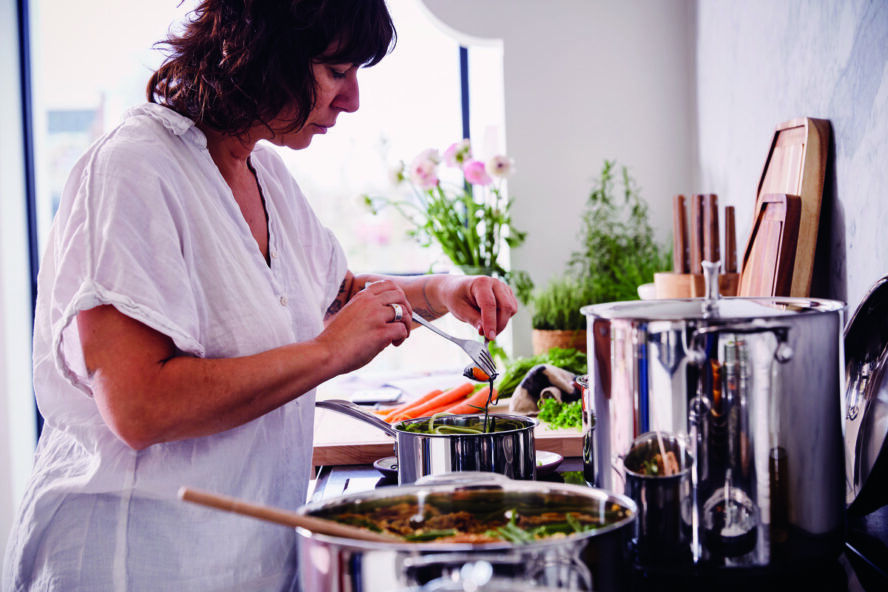 Image of a woman bent over a stovetop with several Alva Cookware Chef Set pieces.