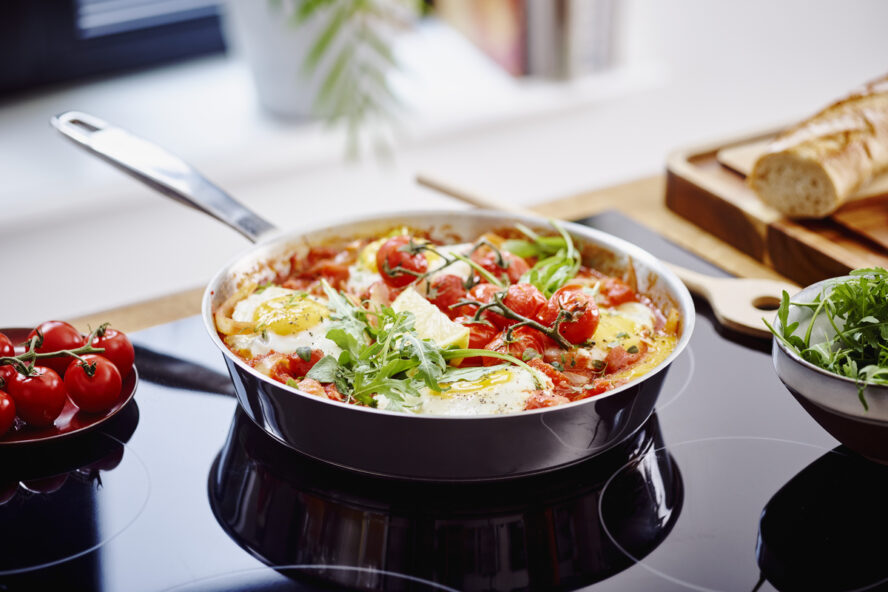 Image of the Alva Maestro 5-ply stainless steel frying pan on a stove, filled with a fresh tomato shakshuka.