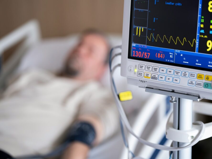 Image of a man hooked up to a machine in a hospital bed, with a screen showing his vital signs.