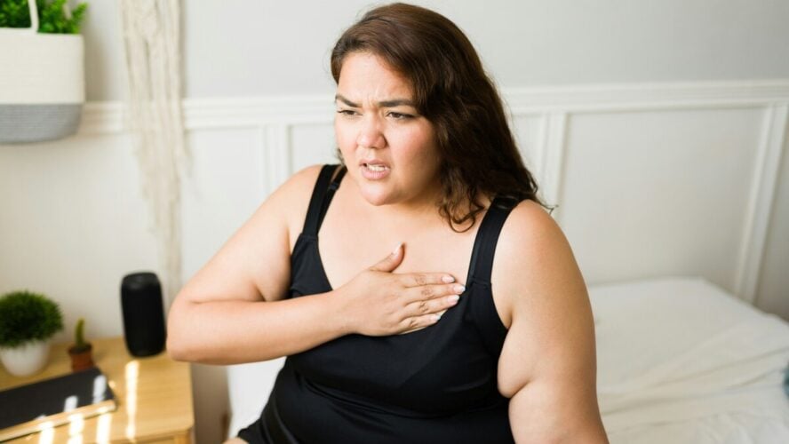 Image of a young woman holding her hand over her heart with an expression of pain on her face.