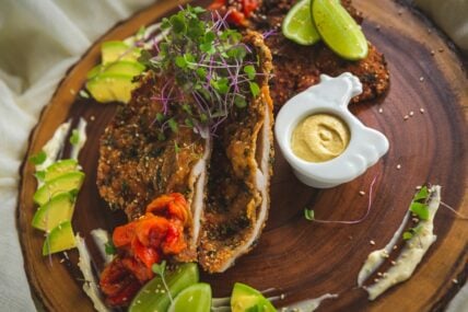 Image of a wooden board with a fried chicken cutlet, mustard, and avocado around it.