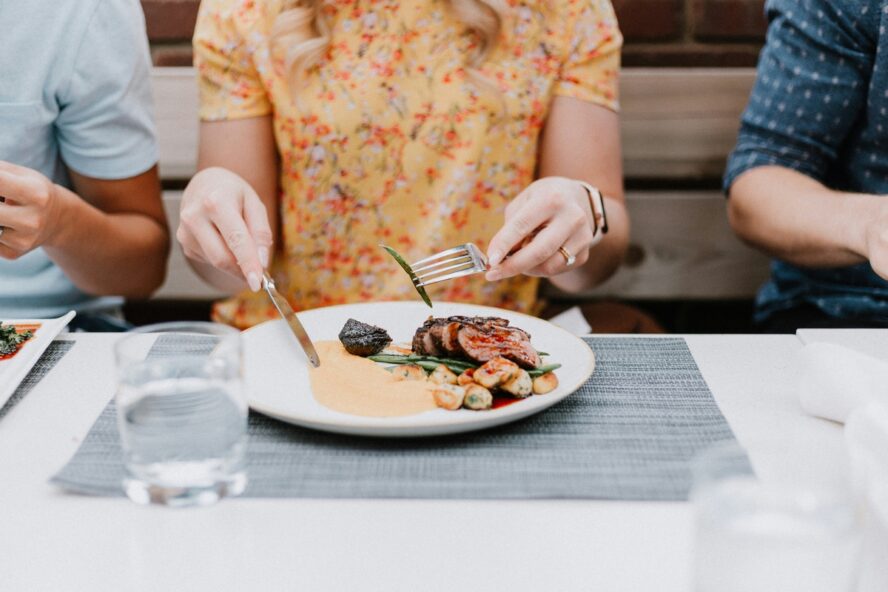 Image of a woman tucking into a plate of steak with asparagus and other veggies.