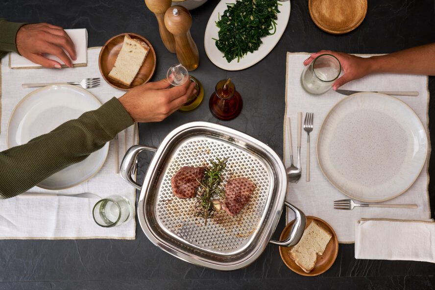 Image of the AbyAMC stovetop grill pan with lid shown being used as a serving pan for steaks on a dining table.