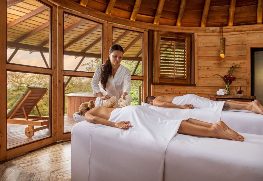 Image of two people lying face-down on spa beds with a masseuse standing behind them.