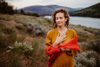 Image of a woman holding her hand over her heart standing outside on a hill overlooking a lake unsplash