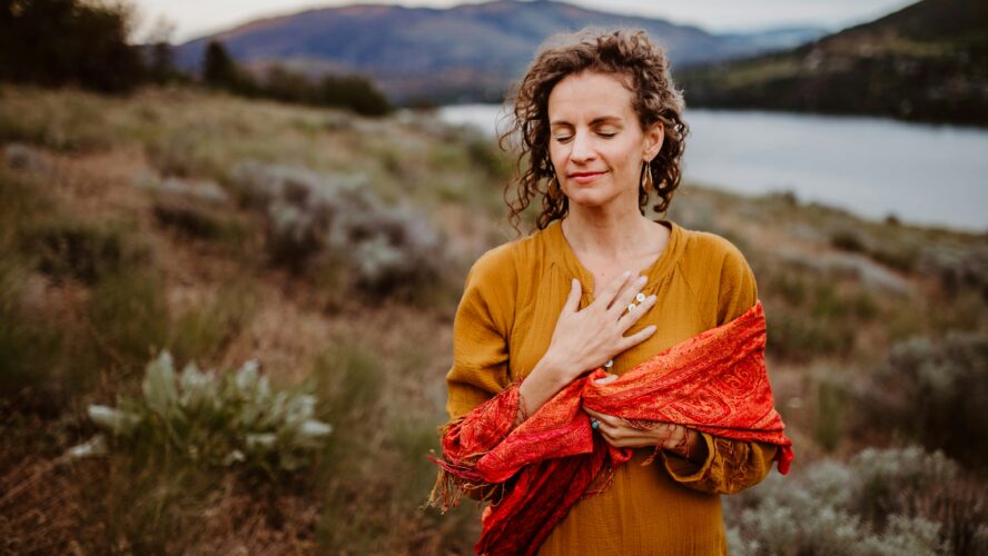 Image of a woman holding her hand over her heart standing outside on a hill overlooking a lake unsplash