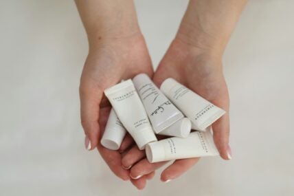 Image of a woman's hans holding travel shampoo bottles of which may contain phthalates. anna keibalo nbiIuy unsplash
