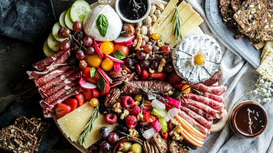 Image of an abundant holiday cheese board with various cheese types, fruit, delicate meats, and spreads.