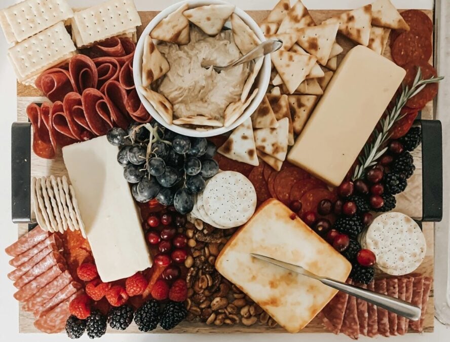 Image of a beautiful cheese and charcuterie board on a wooden slab.