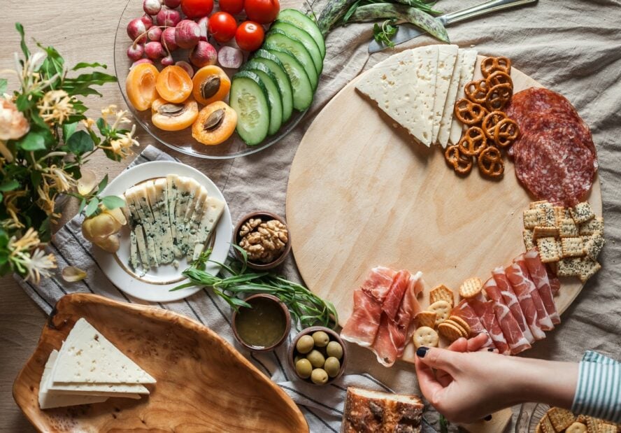 Image of a gorgeous table with a round wooden slab and an array of colorful cheeses and fruits.