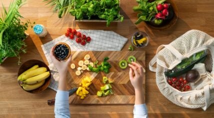 Image of a pair of hands shown from above, preparing some high-fiber fruit and vegetables on a wooden cutting board.