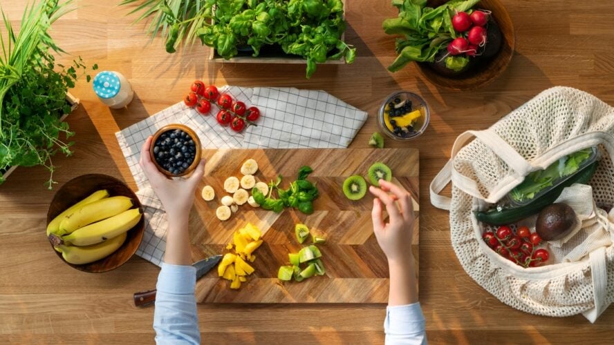 Image of a pair of hands shown from above, preparing some high-fiber fruit and vegetables on a wooden cutting board.