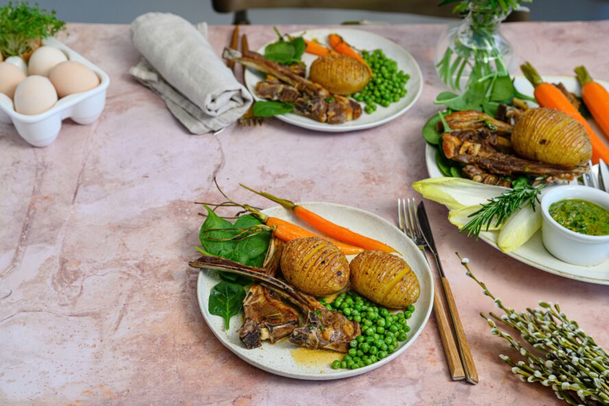 Image of two dinner plates with a lamb shank, potatoes, peas, carrots, and greens.