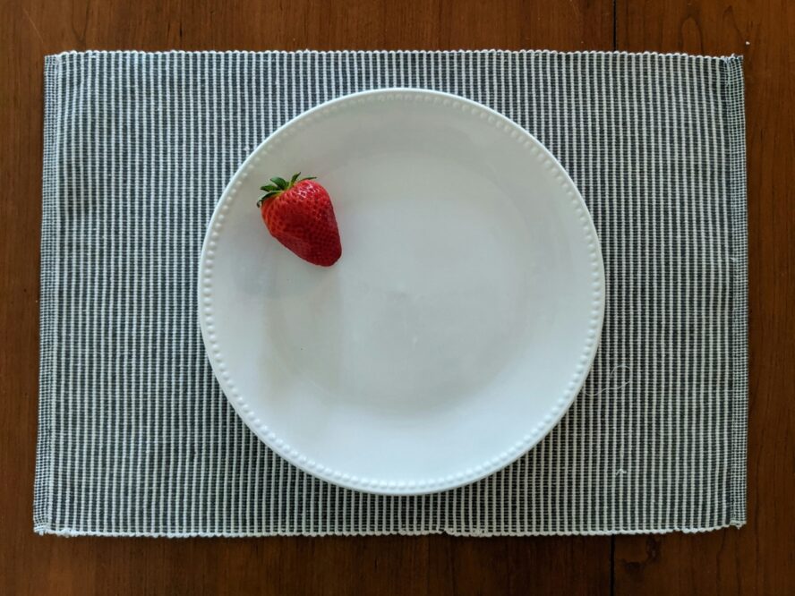 Image of a white plate on a striped placemat with a single strawberry on it.