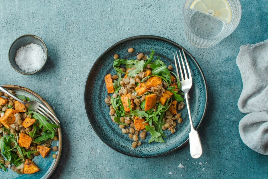 Image of a blue plate featuring a sweet potato salad with lentils and arugula.