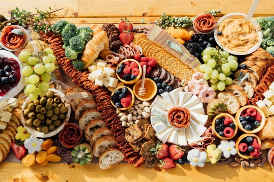 Image of a colorful cheeseboard shown as a table centerpiece, with layers of crackers, cheese, fruit, and more.