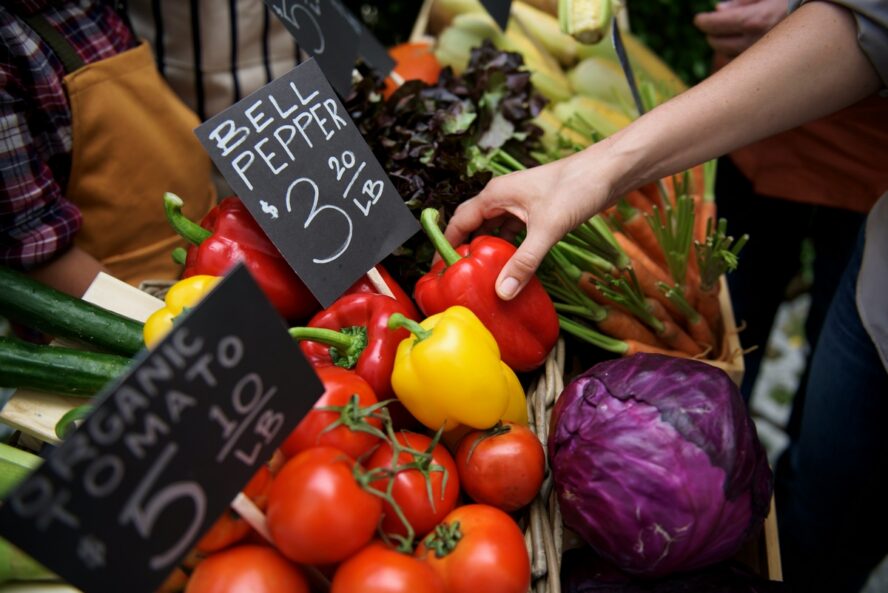 Image of wooden crates of bell peppers at a farmer's market with a pair of hands reaching for a red pepper.
