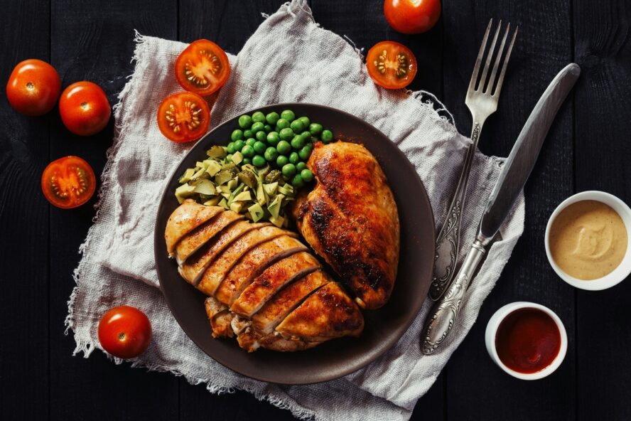 Image of a plate with a heaping portion of roasted chicken alongside peas and other greens.
