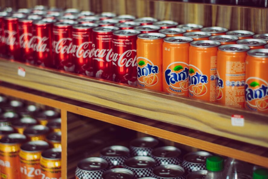 Image of rows of colorful cans of soda shown in a grocery store.