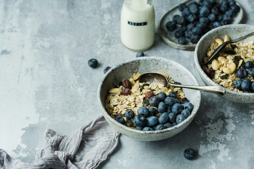 Image of a bowl full of dry oats and blueberries, set next to a bottle of Kefir.