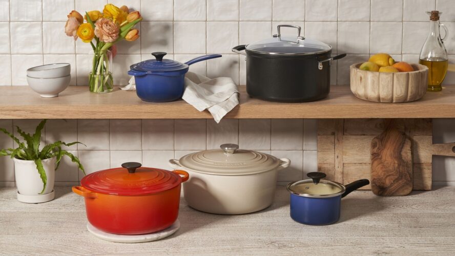 Image of several Le Creuset pieces shown in vibrant colors on open shelving.