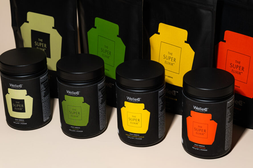 Image of several WelleCo The Super Elixir tubs and flatpacks in different flavors lined up next to each other.