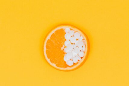 Image of a slice of orange laid flat, with half of the fruit replaced with small white supplement pills.