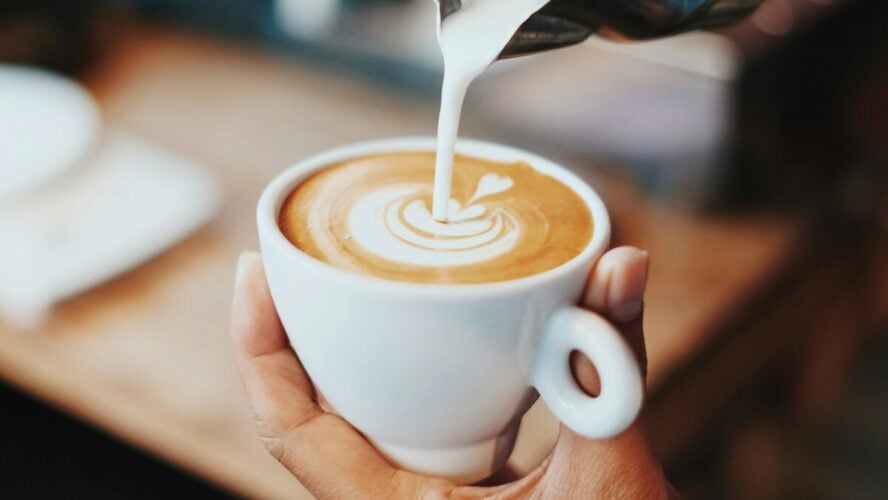 Image of a barista pouring steamed milk into a coffee cup to create latte art.