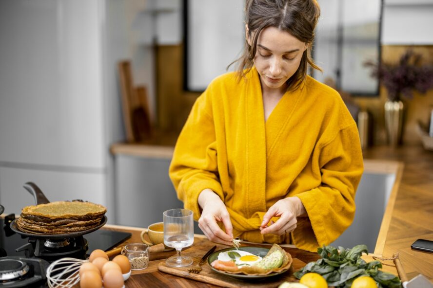 Image of a woman in a yellow bathrobe preparing a plate of breakfast with eggs for herself.