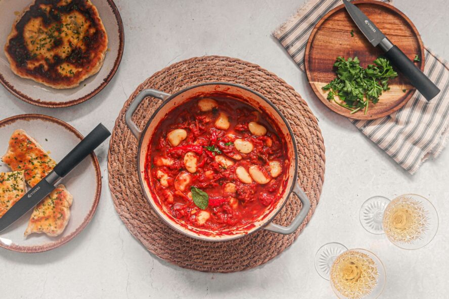 Image of a small bowl full of a tomato-based soup filled with chunky white beans.