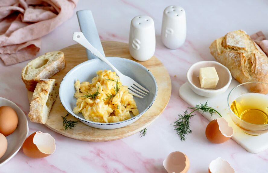 Image of a small bowl of scrambled eggs, alongside a salt and pepper shaker and a small cup of butter.