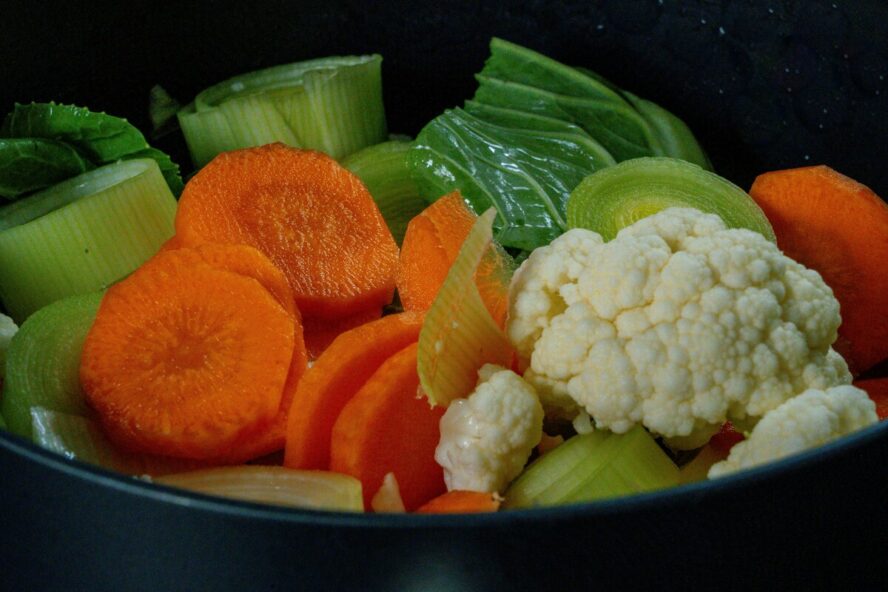 Image of many colorful steamed vegetables, including carrots, cauliflower, and leeks.