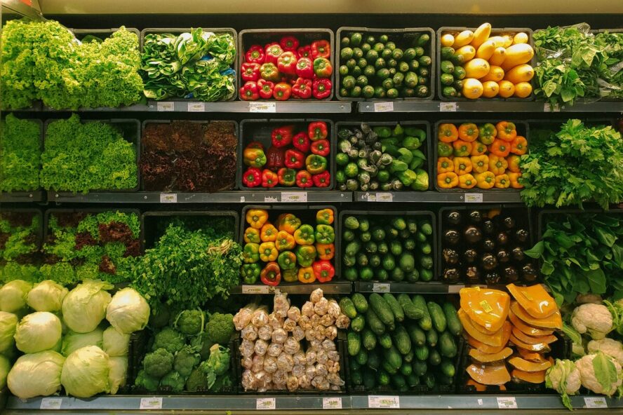 Image of the fresh produce aisle in the grocery store, showcasing rows of peppers, cucumbers, and other vegetables.