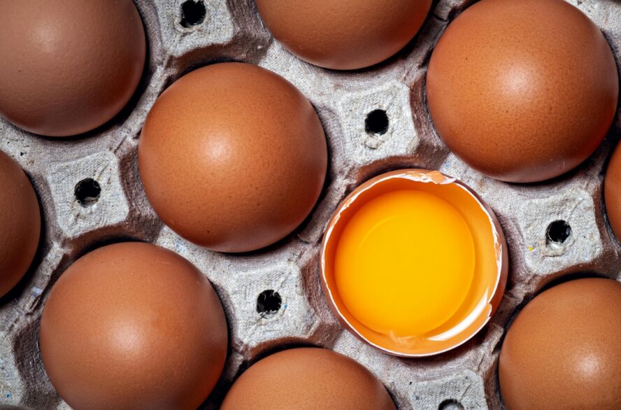 Close-up image of a carton of eggs, showing one cracked open to reveal the yolk inside.