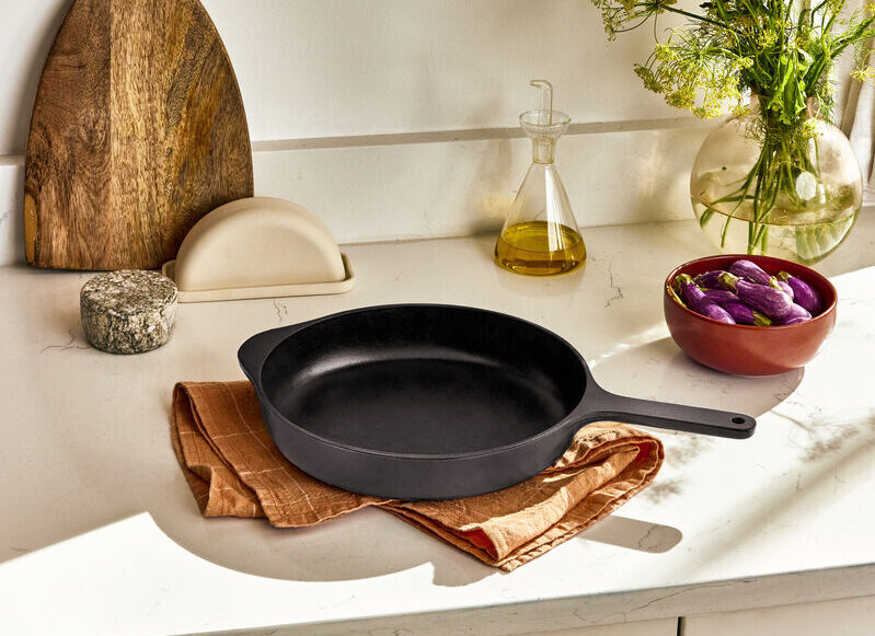 Image of the Caraway enameled cast iron skillet in midnight blue, resting on an orange napkin on a white marble countertop.