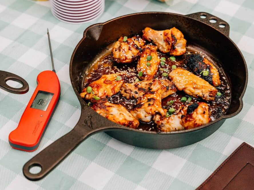 Image of the Smithey No. 10 Skillet with chicken wings in a sticky glaze, shown on a picnic table.