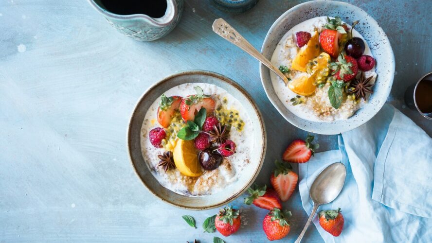 Image of two small bowls full of oatmeal, topped with various berries and tropical fruits.