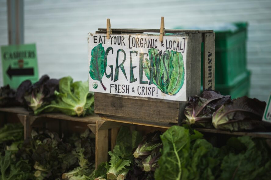 Image of a sign advertising organic, local greens at a farmer's market, with said greens displayed around the sign.