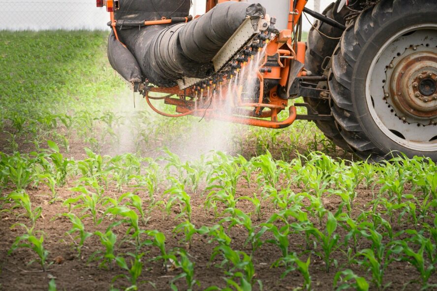 Image of a tractor spraying pesticides over a field of growing crops.