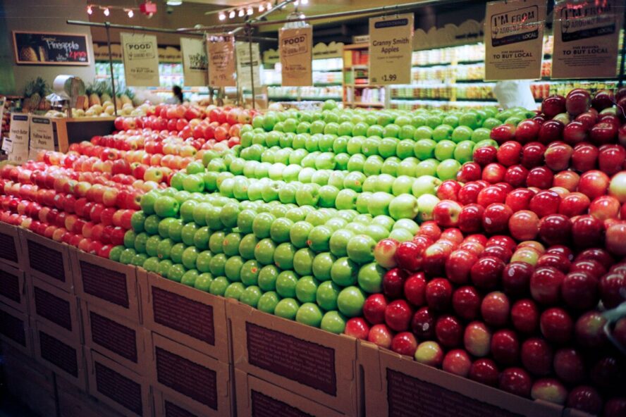 Image of a produce section at a grocery store, featuring piles of green and red apples.