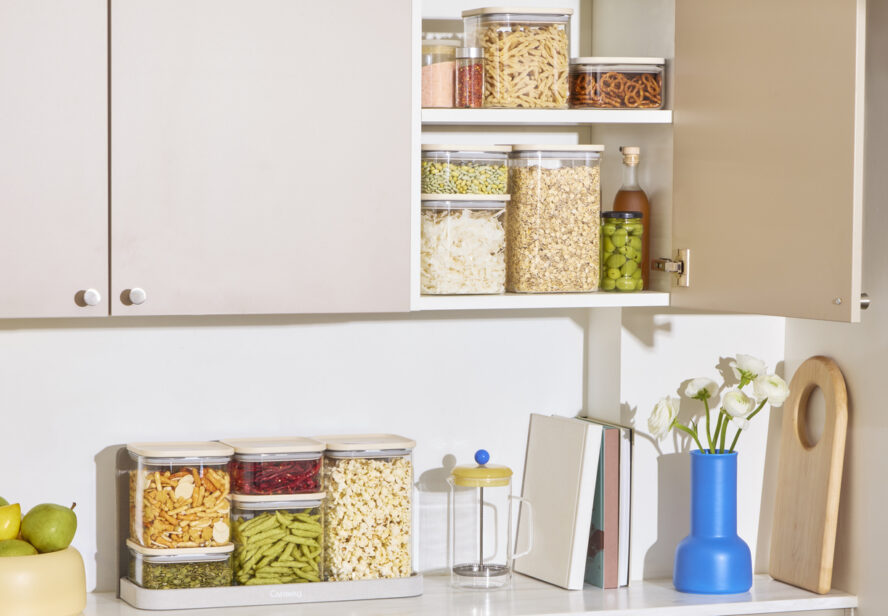 Image of a kitchen countertop with storage above it with the doors open, showcasing several Caraway Glass Airtight Food Containers on both the counter and in the cupboards.