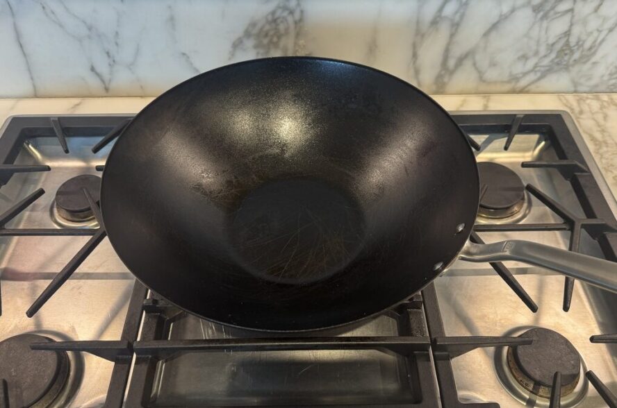Image of the Made In Seasoned Carbon Steel Wok on a gas stovetop against a white marble backsplash.