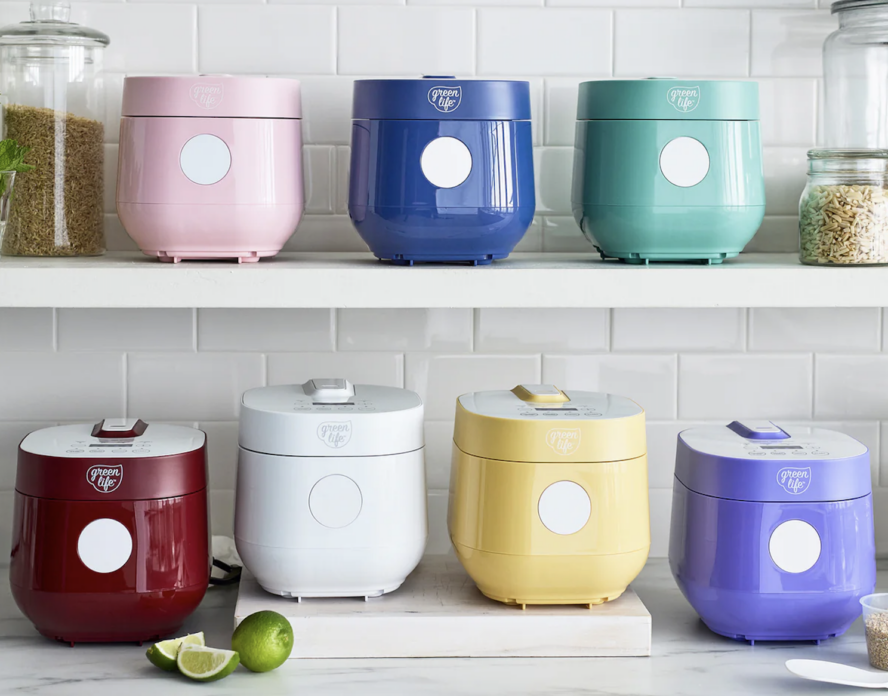 Image of several GreenPan GreenLife Rice & Grains Cookers in various colors lined up on two shelves in a white kitchen.