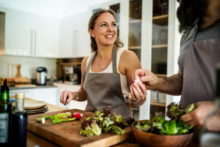 Image of a smiling woman wearing an apron and chopping vegetables on a cutting board. 