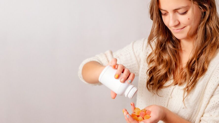 Image of a young woman pouring a bottle of gummy vitamins into her hand.