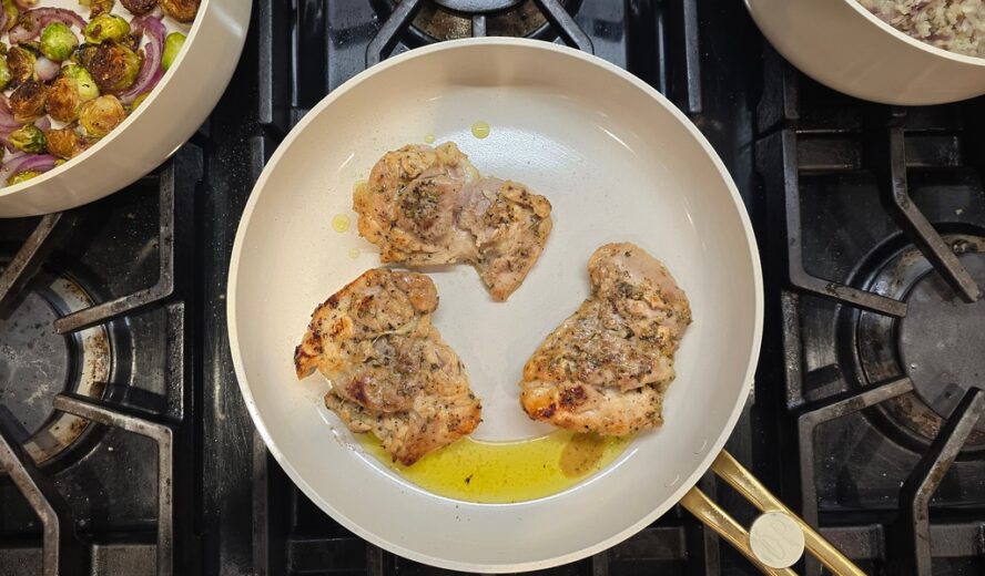 Image of an Our Place Essentials fry pan on a stovetop being used to cook three seared chicken thighs.